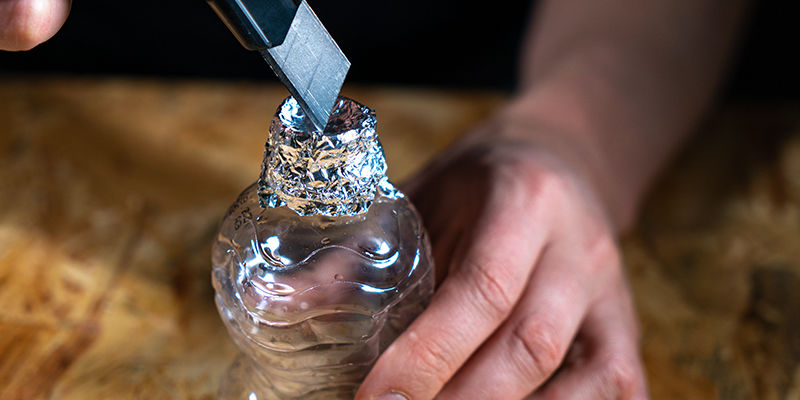 Ta av kapsylen och vira aluminiumfolie runt toppen på den första flaskan Gravitationsbong i hink: Ta av kapsylen och vira aluminiumfolie runt toppen på den första flaskan